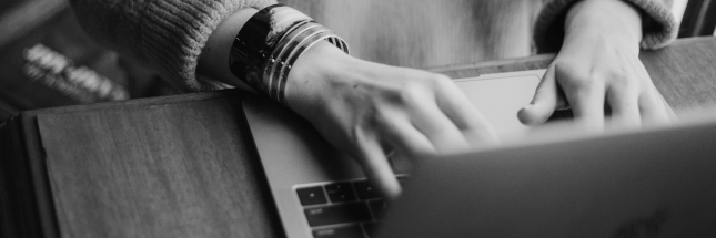 Imagem em preto e branco com notebook visto de cima com mãos no teclado